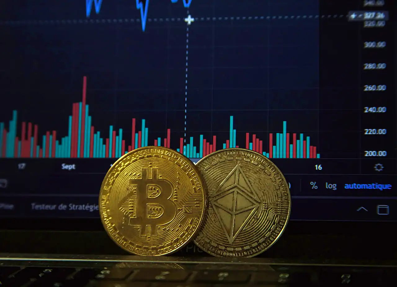 Ilustrasi: Dua keping mata uang kripto (crypto) di depan sebuah layar monitor. (Foto: Unsplash/Pierre Borthiry)